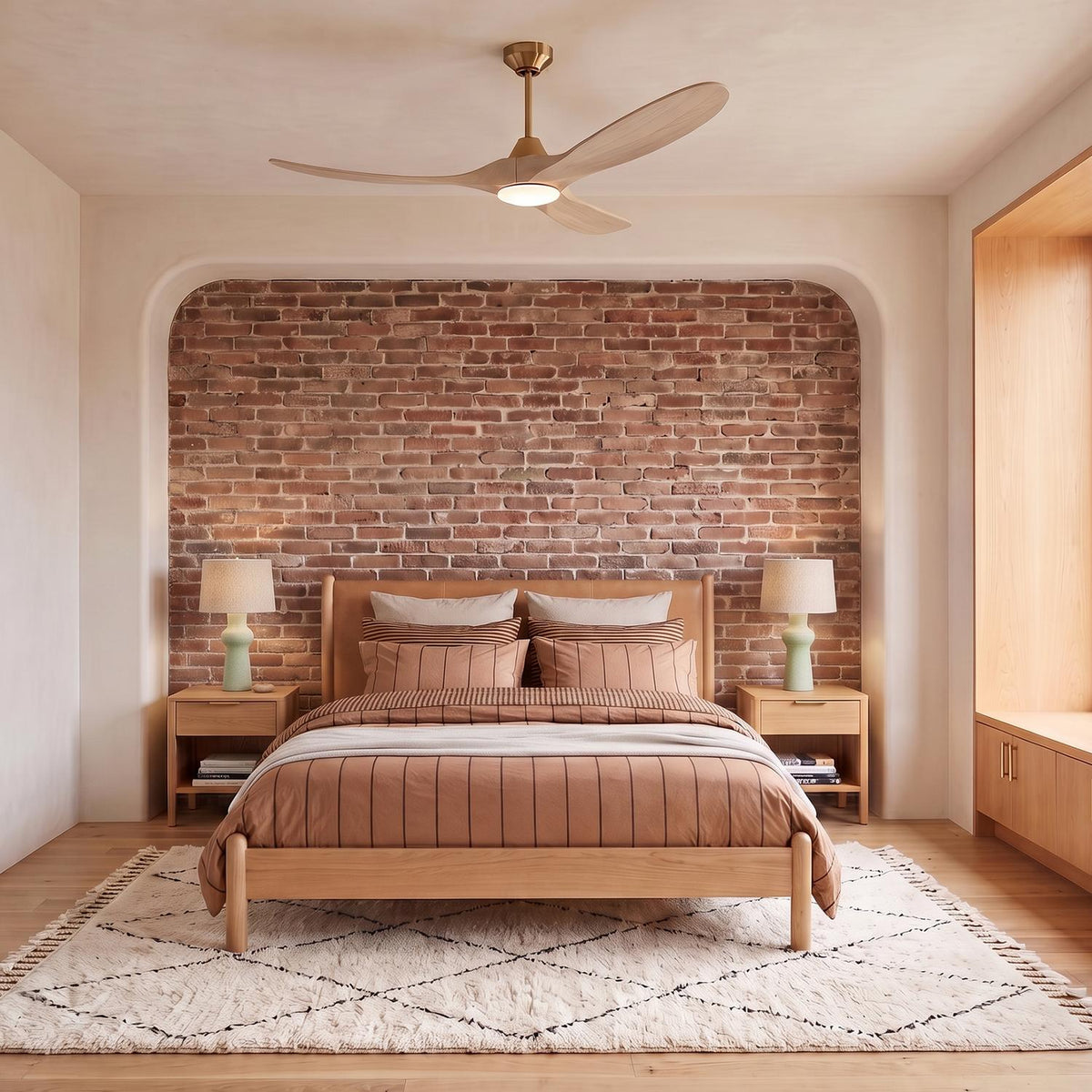 A modern bedroom with the Egret LED Ceiling Fan 60" in whitewash oak and modern brass installed above a wood bed and brick accent wall.