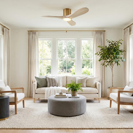 A modern living room with the Eider LED Ceiling Fan 44", Whitewash Oak and Modern Brass, mounted in the ceiling center above a beige sofa and grey ottoman.