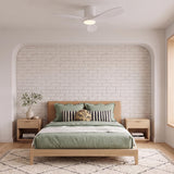 A modern bedroom featuring the Eider LED Ceiling Fan 44", Matte White Oak along the ceiling center over a wood bed with sage green linens and white brick.