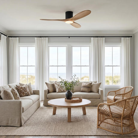 A coastal living room with the Eider LED Ceiling Fan 52", Natural Oak and Matte Black mounted to the ceiling above rattan armchairs and neutral sofas.