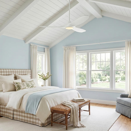 A coastal bedroom with an Egret LED Ceiling Fan 52" in matte white oak installed on a vaulted beamed ceiling above a tan gingham upholstered bed.
