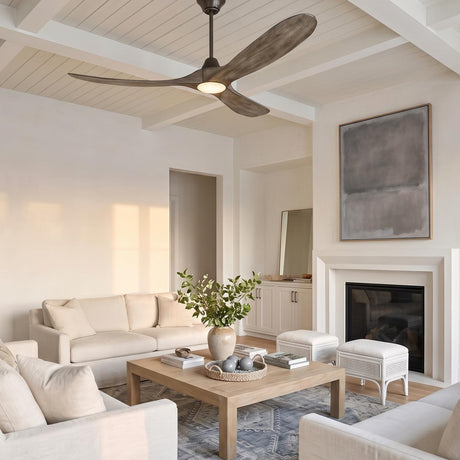 A modern living room with the Egret LED Ceiling Fan 60 in gray wash oak and aged pewter on a beamed ceiling above white sofas and a fireplace.