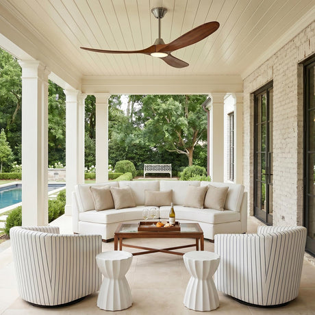 A modern farmhouse porch featuring the Egret LED Ceiling Fan 60" in koa wood and brushed steel mounted above a curved white sectional and white brick walls.
