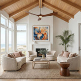 A coastal living room features an Egret LED Ceiling Fan 70" in koa wood and brushed steel installed on a vaulted ceiling above white boucle sofas.