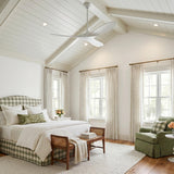 A cottage bedroom with the Egret Ceiling Fan 52", Matte White Oak, on a vaulted shiplap and beamed ceiling above a green gingham bed.