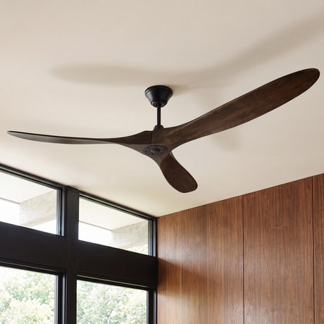 A mid-century living room with the Egret Ceiling Fan 88", Walnut Wood and Matte Black mounted near vertical wood wall paneling and large black-framed windows overlooking outdoor greenery.