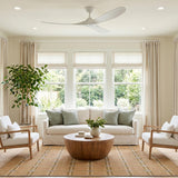 A transitional living room with an Egret Outdoor Ceiling Fan 60", Matte White on the white ceiling above large windows, featuring a tan plaid rug and potted tree.