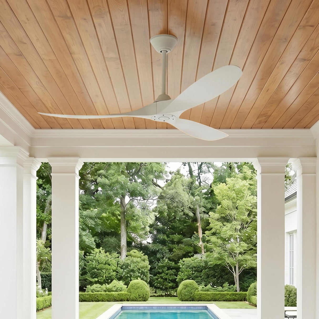 A modern farmhouse porch with a wood-plank ceiling featuring the Egret Outdoor Ceiling Fan 60" in matte white overlooking a swimming pool and manicured boxwood.