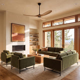 A modern living room featuring Egret Ceiling Fan 60", Natural Oak and Matte Black with natural oak blades installed above olive green velvet sofas and a modern fireplace.