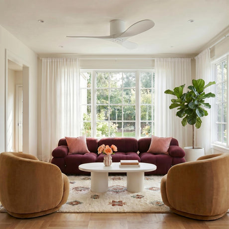 A contemporary living room with the Eider Ceiling Fan 44" in Matte White Oak along the ceiling center above a burgundy sofa and ochre swivel chairs.