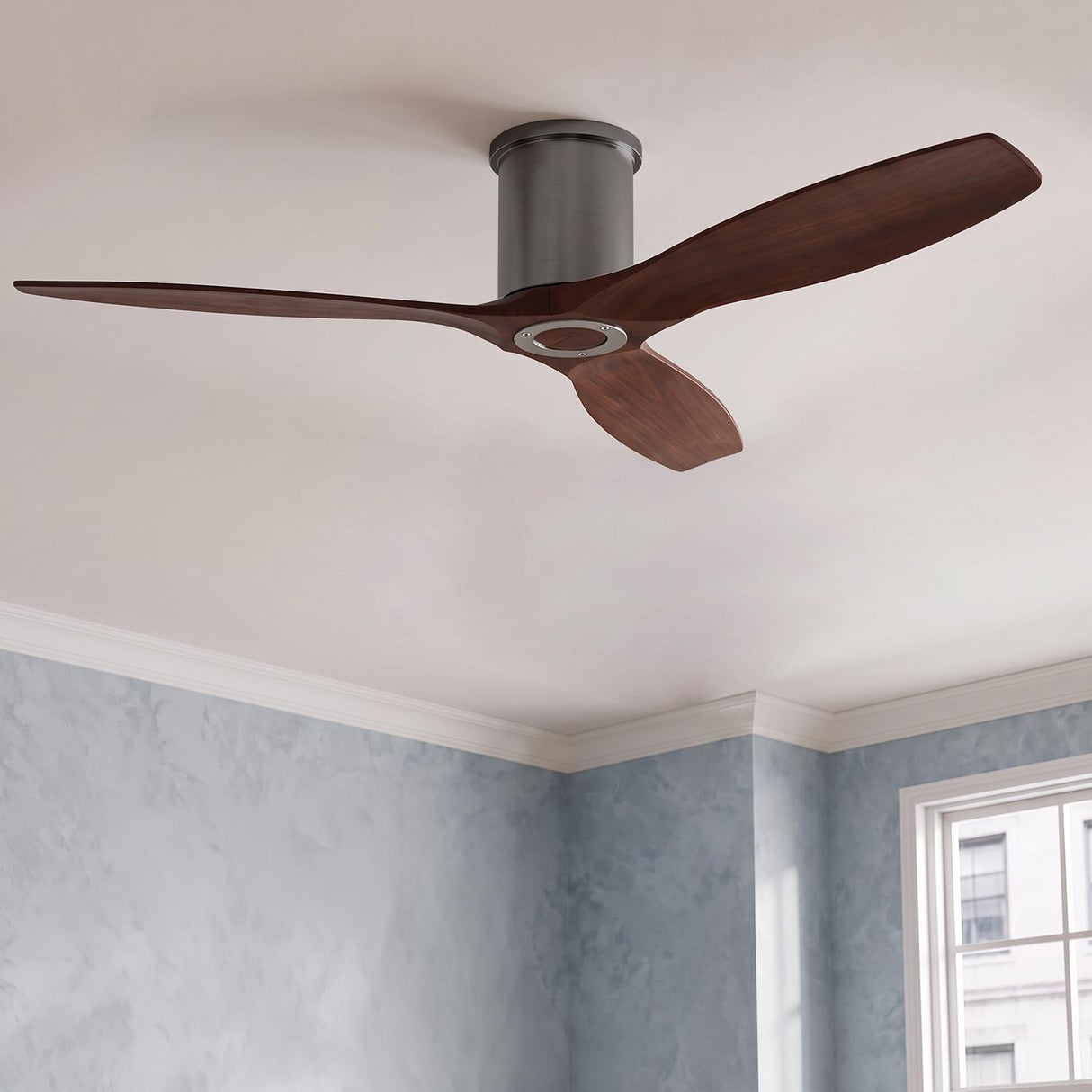 A modern bedroom featuring the Harrier Smart Ceiling Fan 52 inch with walnut wood blades and brushed steel housing mounted to a standard ceiling beside blue textured walls.