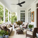 A coastal porch with the Heron Outdoor Smart Ceiling Fan 52", Matte Black on a white beadboard ceiling, featuring white siding and wicker seating with palms.