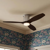A transitional bedroom featuring the Harrier LED Smart Ceiling Fan 52", Walnut Wood and Brushed Steel, on a standard ceiling beside blue floral wallpaper and cream crown molding.