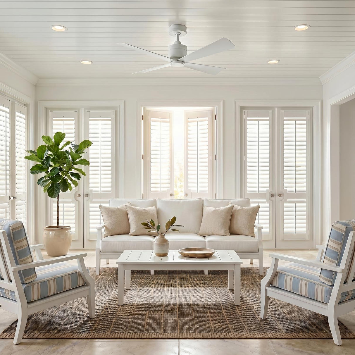 A coastal living room featuring the Sora Ceiling Fan 44", Matte White mounted on a white shiplap ceiling above a white sofa and a fiddle leaf fig.