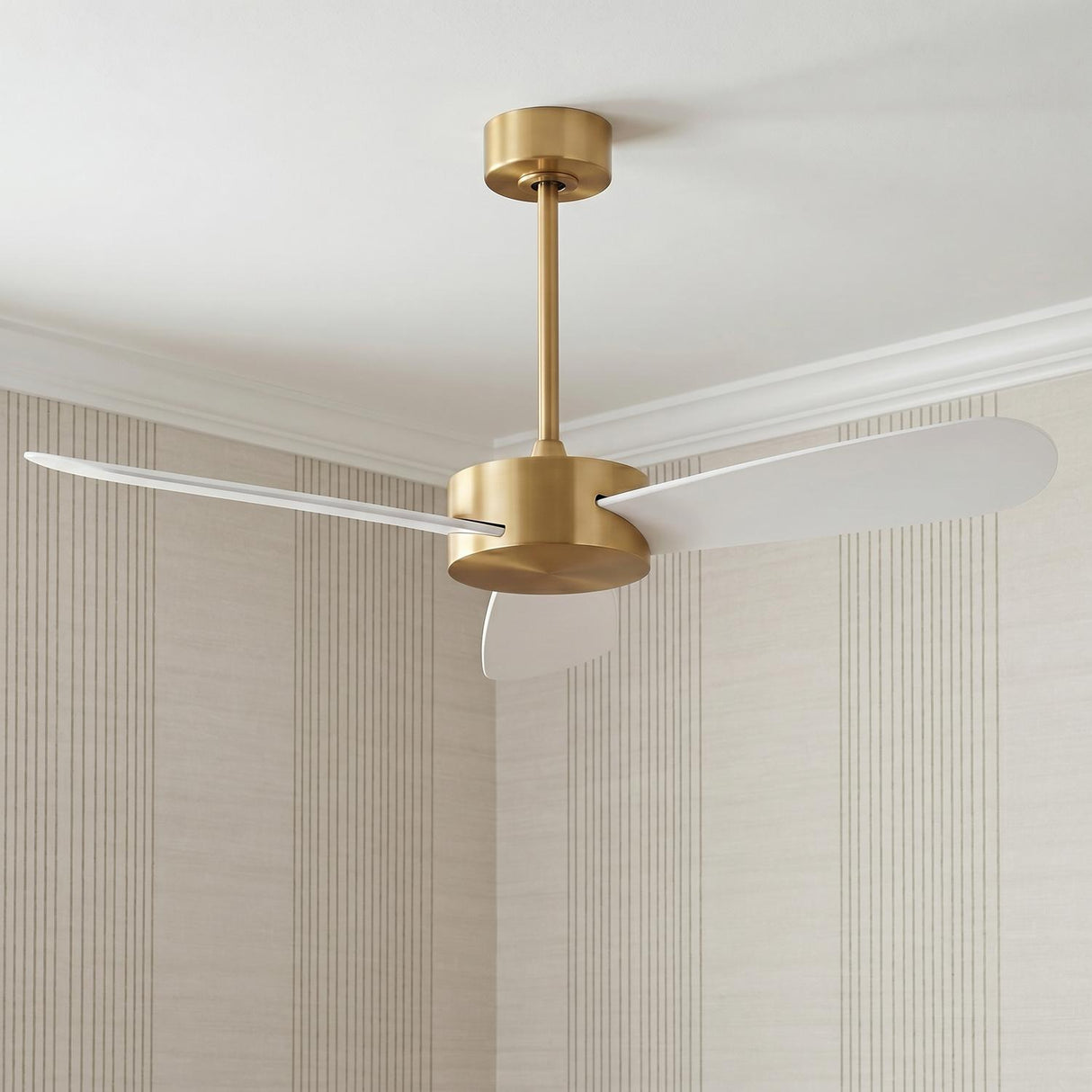 A modern living room with the Willet Smart Ceiling Fan 52 inch in modern brass and matte white mounted on the ceiling against striped wallpaper.