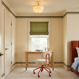 A traditional bedroom features the Cortland Semi-Flush 14", Champagne Glass and Aged Brass fixture centered on the ceiling above a wood desk and green roman shade.