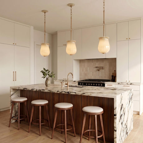 A transitional kitchen with three Cortland Small Pendants in ribbed champagne glass and aged brass over a marble waterfall island with dark wood slats and white cabinets.