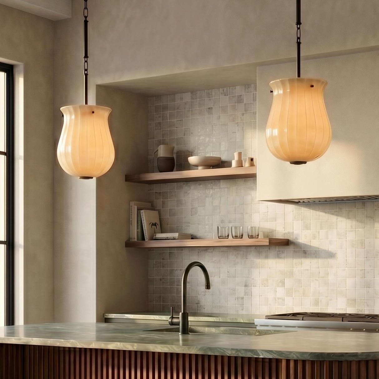 A transitional kitchen with two Cortland Small Pendants in champagne glass and distressed bronze over a green marble island countertop with visible tile and floating shelves.