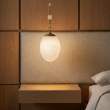 A modern bedroom featuring the Kelton Small Pendant 8", Cloud Glass and Aged Brass hanging over a floating wood nightstand beside a linen textured headboard.