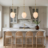 A transitional kitchen with three Kelton Medium Pendants in cloud glass and aged brass over a white marble waterfall island and light wood counter stools.