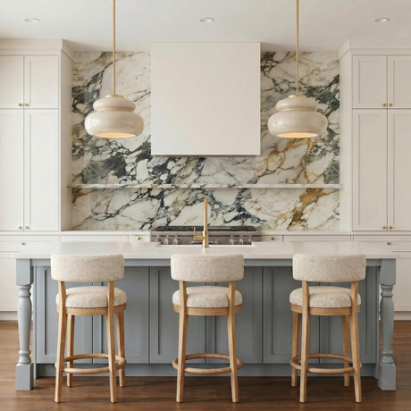 A transitional kitchen with two Ellsworth Pendants in taupe crackle ceramic and aged brass over a white island featuring a dramatic marble backsplash and light blue cabinetry.