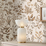 A traditional bedroom featuring the Dorset Table Lamp 17 inch with fluted cloud glass and aged brass sitting on a light oak dresser with botanical wallpaper.
