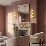 A traditional living room featuring the Bristolia 3 Light Wall Sconce in aged brass and clear piastra glass flanking a mirror above a marble fireplace.