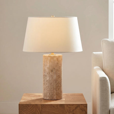 A contemporary living room with the Cassian Table Lamp featuring a fluted travertine base and linen shade on a wood side table beside a cream sofa.