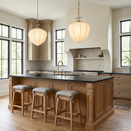 A transitional kitchen features two Chiya Large Pendants with vintage brass and white silk shades suspended over a wood island with black countertops and striped stools.