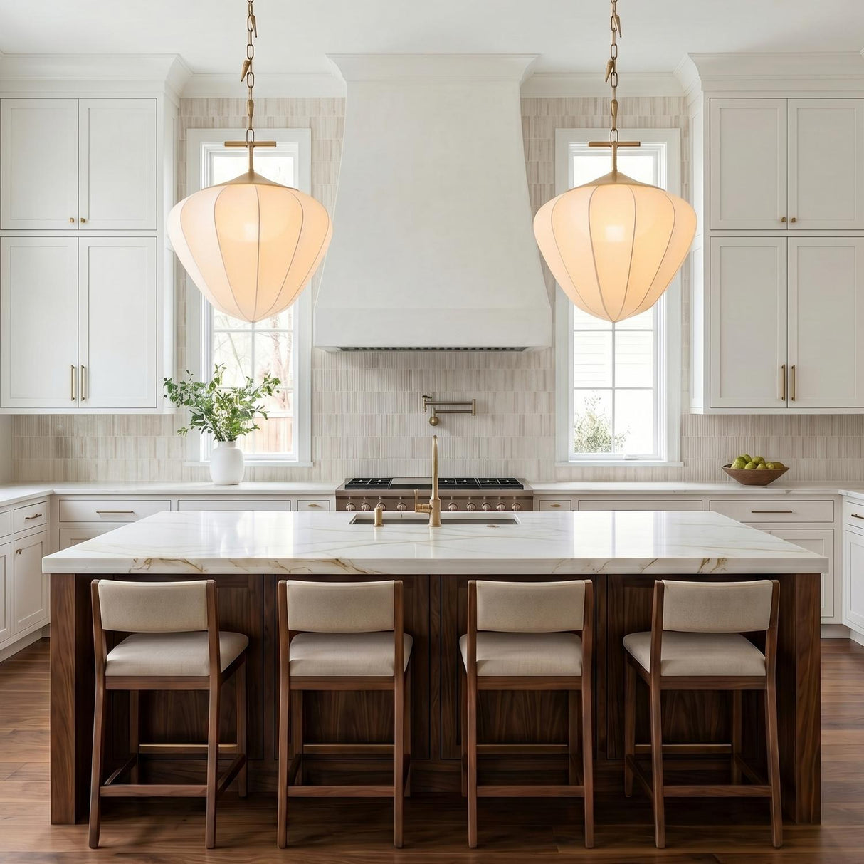 A transitional kitchen with two vintage brass and white silk pendants hanging over a white marble island with dark wood base and vertical tile backsplash.