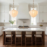 A transitional kitchen with two vintage brass and white silk pendants hanging over a white marble island with dark wood base and vertical tile backsplash.
