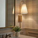 A traditional bathroom with the Wynn Wall Sconce 24", Vintage Brass featuring a white pleated linen shade mounted beside a brass-framed mirror and marble vanity.