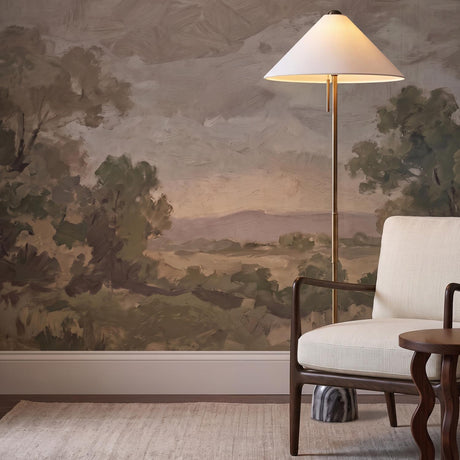A transitional living room features the Hendrix Floor Lamp 64", Gray Marble and Patina Brass with a white cone shade beside a cream armchair and landscape mural.