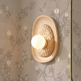 A transitional bathroom with a Sybella Wall Sconce in beech wood and aged brass featuring a hand-carved texture and globe bulb on floral wallpaper beside a mirror.