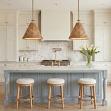 A farmhouse kitchen with two braided jute and patina brass pendants over a white marble island featuring blue shaker cabinetry and a chevron marble tile backsplash.