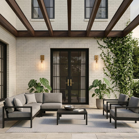 A modern farmhouse patio with Webster Outdoor Wall Lights in patina brass flanking black glass doors on white brick with ivy at twilight.