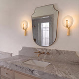 A modern bathroom with two gold leaf Zahara LED Wall Sconces with alabaster discs flanking a shaped mirror above a grey marble countertop and gold faucet.