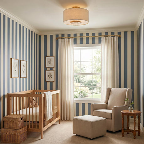 A transitional bedroom with blue and white striped wallpaper and a Wolfe Medium Semi-Flush in ivory boucle and aged brass installed above a light wood crib.