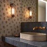 A transitional bathroom featuring vintage bronze wall sconces with ribbed glass shades flanking a mirror above a concrete vessel sink and blue zellige tile backsplash.
