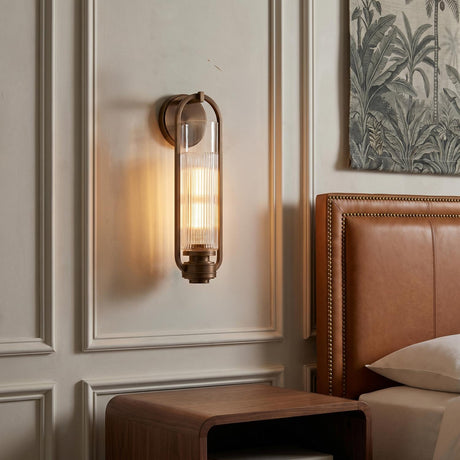 A transitional bedroom featuring the Chatham Wall Sconce 16", Vintage Bronze with ribbed glass mounted on a white paneled wall beside a tan leather headboard.