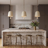 A transitional kitchen with three Briony Medium Pendants in ivory glaze and patina brass suspended over a white marble waterfall island and dark gray cabinetry.