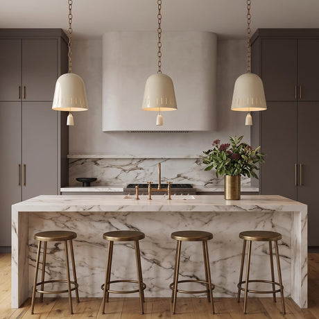 A transitional kitchen with three Briony Medium Pendants in ivory glaze and patina brass suspended over a white marble waterfall island and dark gray cabinetry.