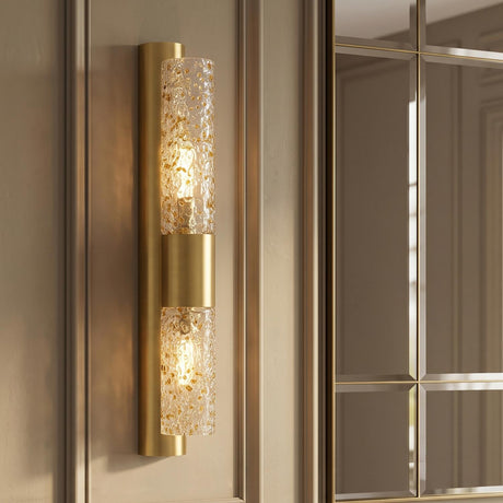 A transitional foyer with the Daylin Wall Sconce 24", Vintage Brass and Amber Speckled Glass mounted on beige paneled walls beside a large gold grid mirror.