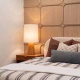 A mid-century bedroom featuring the Gillian Table Lamp with an ivory boucle shade and carved beech wood base on a nightstand against geometric wood wall paneling.