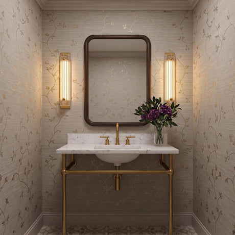 A transitional bathroom with two gold leaf and reeded glass wall sconces flanking a dark wood mirror above a marble console vanity with tan floral wallpaper.