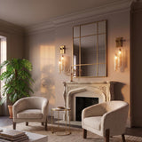A Mediterranean living room with Florencea LED wall sconces in vintage brass and champagne glass flanking a mirror above an ornate stone fireplace and boucle chairs.