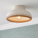 A coastal bedroom featuring the Nadira semi-flush mount in cream ceramic and rattan with aged brass accents above blue grasscloth wallpaper and white molding.