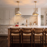A transitional kitchen with two cream and rattan pendants featuring aged brass hardware over a white marble island with woven stools and white shaker cabinets.