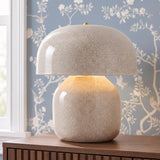 A transitional bedroom featuring the Rayburn Table Lamp 17", Glossy Ivory Slate Crackle on a dark wood dresser against blue floral wallpaper and a white window.