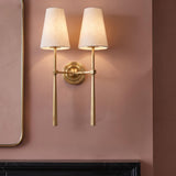 A transitional living room features an Ashlin Double Wall Sconce in vintage brass with linen shades mounted on a dusty rose wall above a black marble mantel.